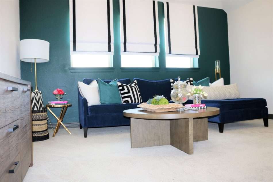 colorful family room, navy sofa, blue sofa, roman shades, black roman shades, green wall, green wall with navy sofa, tripod lamp, coffee table decor